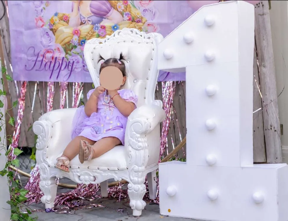 Baby sitting on a small white throne next to a giant number one
