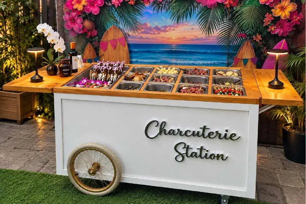 White charcuterie cart filled with snacks in front of a tropical backdrop