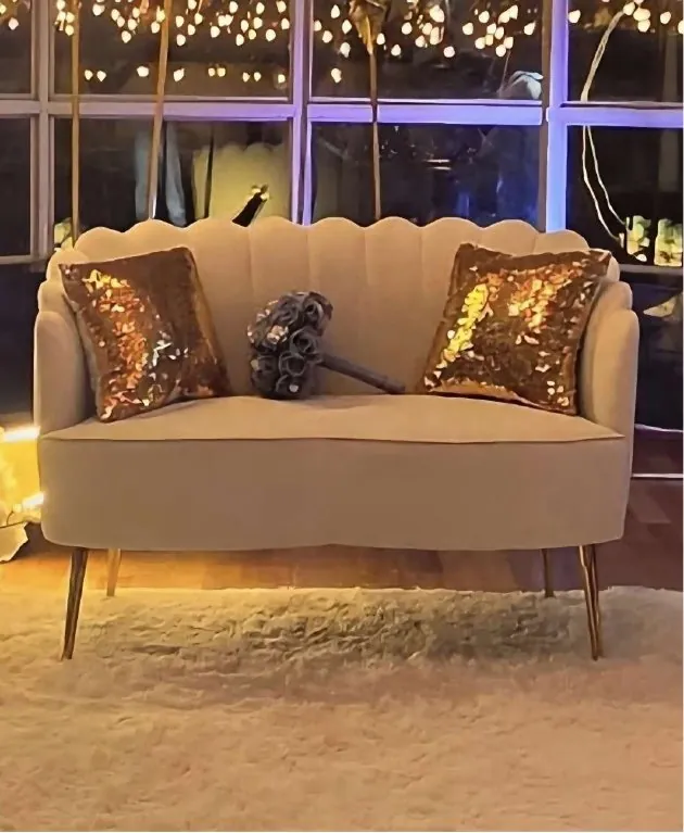 Cream scalloped loveseat with gold sequin pillows under string lights
